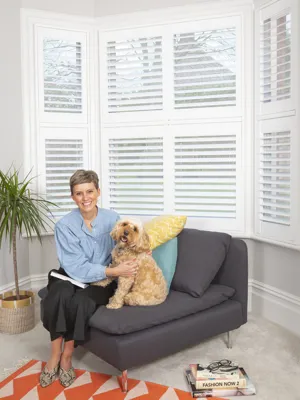 White tier on tier shutters fitted on a bay window in Caroline Macleod's home with her dog