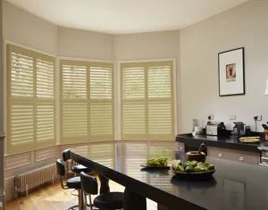 Neutral kitchen with black marble island and worktops and three curved bay windows dressed in French Ochre shutters, louvres opened.