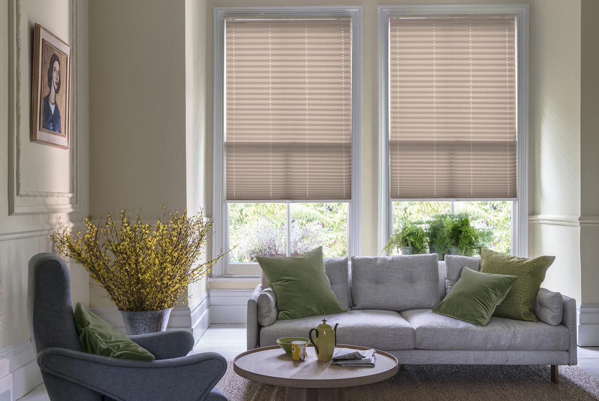 ivory Solartex Chintz Barley Pleated blind are fitted to a series of windows in a kitchen decorated with marble counter tops, white walls and drawers. The Pleated blinds are decorated in a plain style.