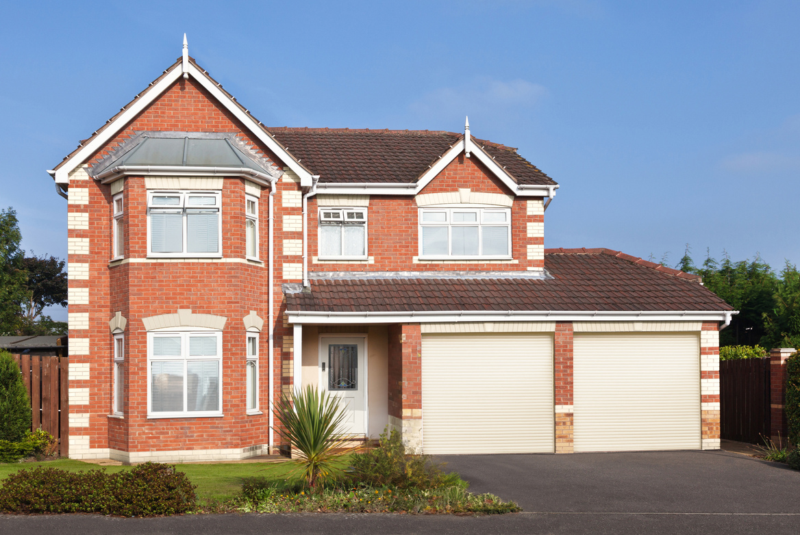 Large house in pale red brick with white arrisses, two integral garage doors in soft white, window frames and guttering in white.