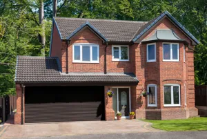 Large traditional brick house with apex windows and double internal garage with dark brown roller door that matches the front door.