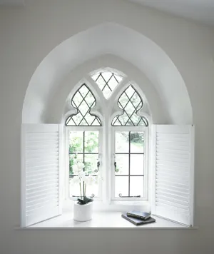 Inset window of small arched with leading on top half in mitre shape with small white shutters to cover the rectangular area, shutters folded back to inset.