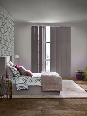 solid tracked shutters in a mid-grey colour in a bedroom with light grey walls and a white feature wall with black patterns