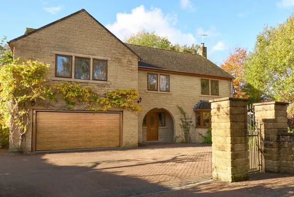 Large Yorkshire-style stone house and drive with integral garage door in mid brown matching front door, with climbing plant above garage.