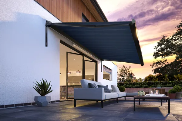 Evening shot of contemporary split level house with patio at bifold doors with grey awning extended over.