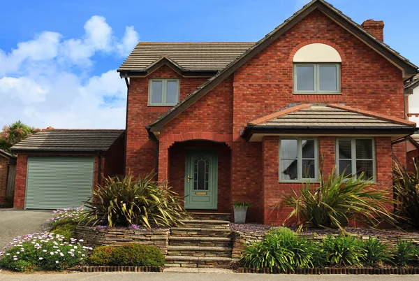 Two storey dark brick house with separate garage with sage green garage door matching front door.