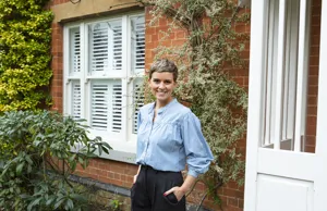 Caroline Macleod standing outside her house with white tier on tier shutters on the inside of the window