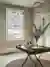 Hallway with wooden floor with round jute rug under folding card table with vase of blue flowers, white stairs to left and window dressed in roller blind with large blue flowers and green foliage
