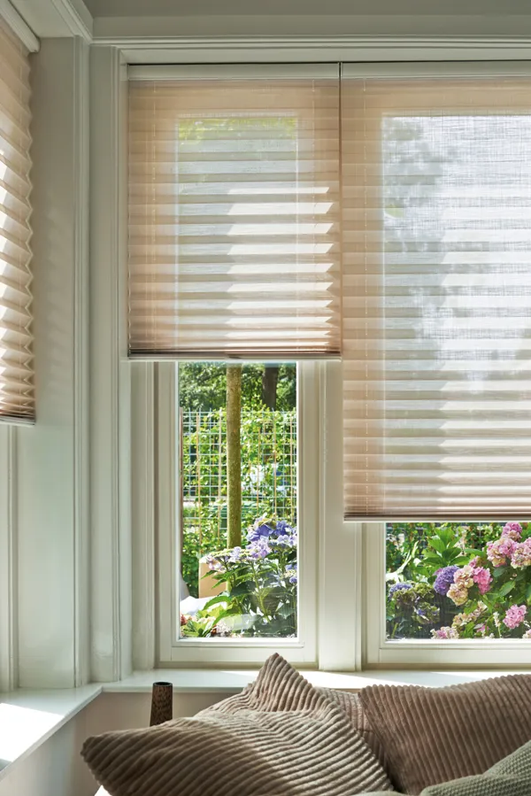 Series of three corner windows dressed in pale peach pleated blinds at varying heights.