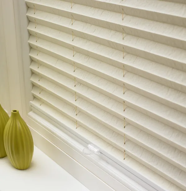 Pale peach marble effect pleated blind lowered, with conical chartreuse-green vase on sill.