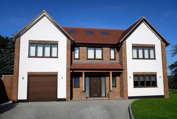 Large contemporary two-tone house with apex windows, integral garage with light brown garage door matching front door.