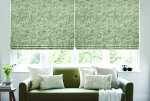 Neutral lounge with olive sofa and white cushions and throw in front of large window dressed in two Roman blinds with a green foliage pattern embroidered on a cream background.