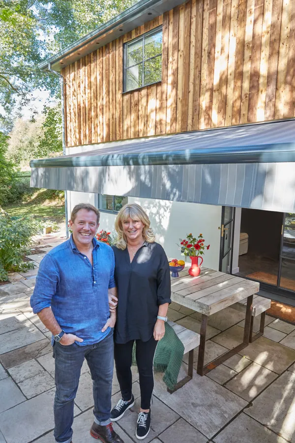 Matt and Lisa Tebbutt stood on their patio with their awning, a table and benches are positioned under the awning