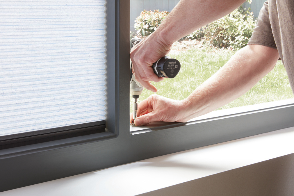 Close up of man screwing fixing for a blind into a window frame interior.