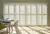 Dining room with contemporary table and chairs on left and large expanse of doors and windows dressed in white tracked shutters, closed with louvres open and light rays on the floor.