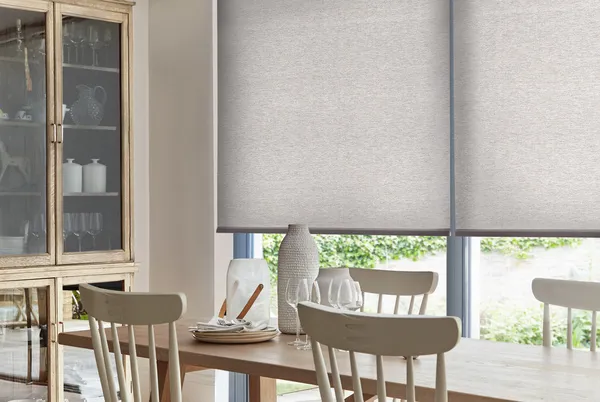 Dining room with bifold doors with mink roller blinds, wooden table and chairs wood and glass sideboard to left with white chine and glassware.