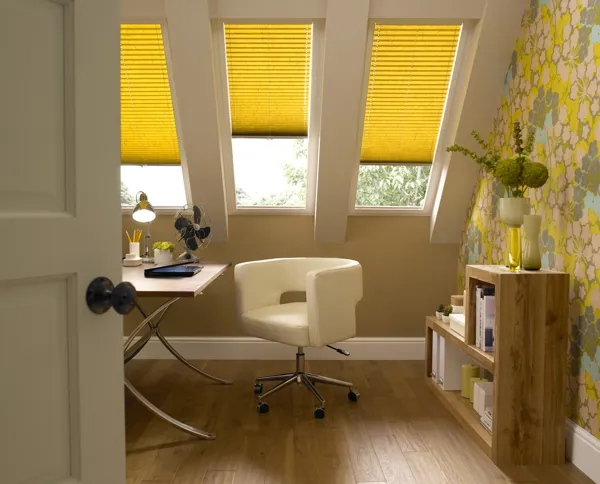 Yellow coloured blinds fitted to skylight windows in a study with a wooden desk, white tub chair and wooden flooring