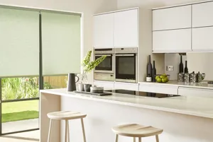 Kitchen in white with touches of green and bifold doors dressed in pale green roller blinds.