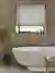 Bathroom with deep recessed window dressed in pale grey-beige roller blind, walls with wood panelling, roll top bath with central mixer taps, small bay tree in pot to left.