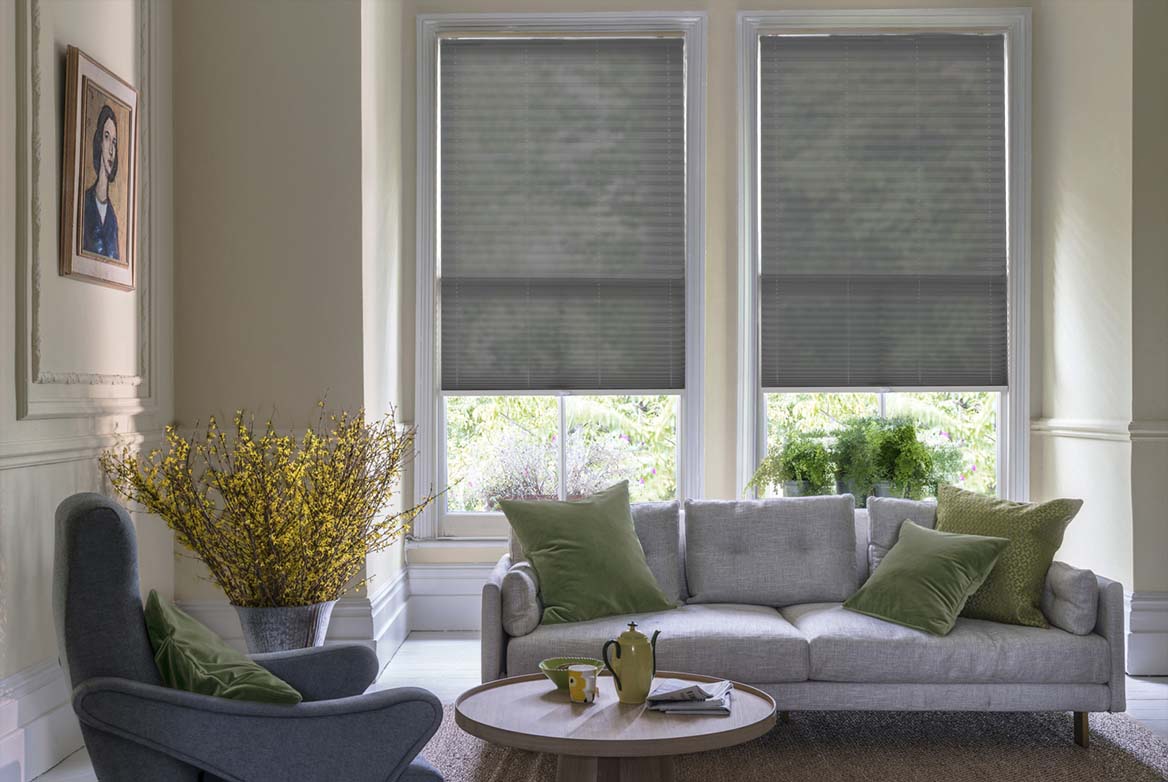 Decorated in a plain style Lumina Sheer Mercury grey Pleated blinds are fitted to windows in a kitchen with marble counter tops and cream coloured fixtures.
