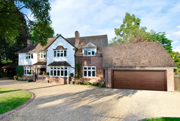 A large detached property with a garage attached with a brown sectional garage door and a shingle driveway.