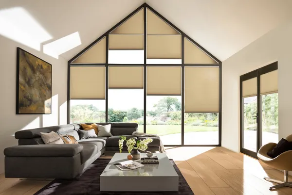 Living area with grey sofa and low table on a rug over a wooden floor with gable end dressed in pale caramel duette blinds at varying levels.