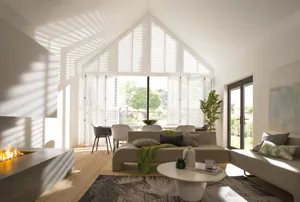 Neutral lounge with feature fireplace, lit, with beige sofas, contemporary table and chairs in front of gable end windows and doors dressed in white shutters.
