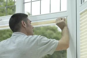 A blinds installer fits an ivory pleated blind into a bay window.