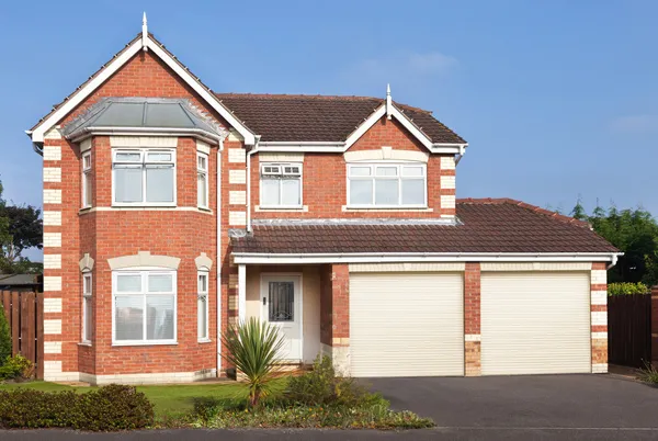 Large house in pale red brick with white arrisses, two integral garage doors in ivory, window frames and guttering in white.