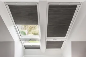 Two adjacent skylight windows dressed in dark grey blinds, left raised and right lowered and beneath two smaller windows dressed the same, left cafe style right extended.