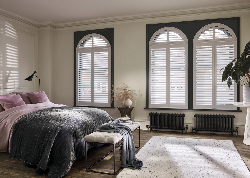 Arched white shutters in bedroom with white rug and grey and pink furnished bed
